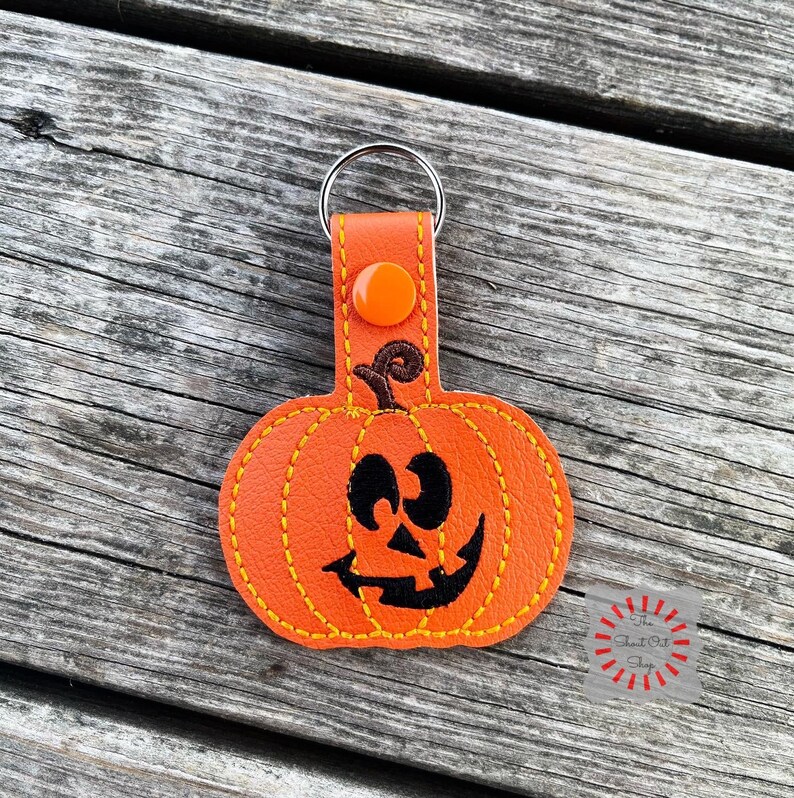 May include: Orange leather pumpkin keychain with a stitched black jack-o'-lantern face and a silver key ring.
