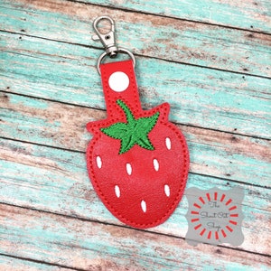 May include: Red leather strawberry keyring with green embroidered leaves and white embroidered seeds. The keyring has a silver metal ring.
