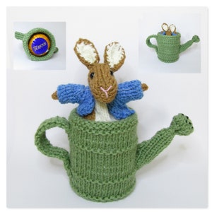 May include: A knitted green watering can with a brown rabbit wearing a blue sweater inside. The watering can has a brown handle and a long spout.