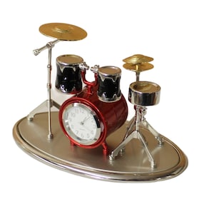 Op de afbeelding: Een rode en zilveren miniatuur drumset klok met een witte wijzerplaat en zwarte wijzers. De klok is opgezet als een echte drumset met een basdrum, twee toms, een bekken en een hi-hat.