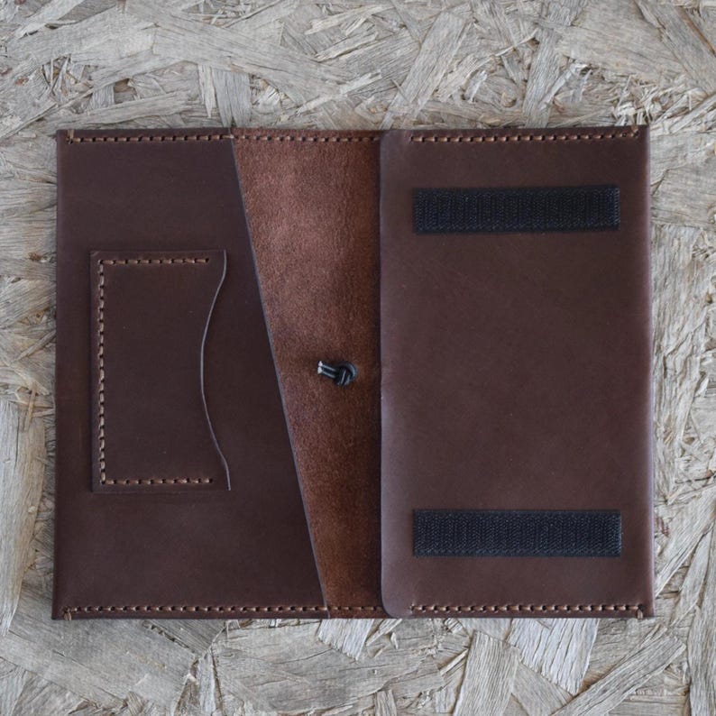 May include: Open brown leather wallet with a card slot and a button closure. The wallet has a contrasting lighter brown interior and two black velcro strips for closure. The edges are stitched with a darker brown thread.