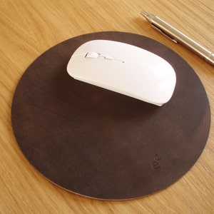 May include: A brown leather mouse pad with a white wireless mouse on top. The mouse pad has a circular shape and a slightly textured surface.