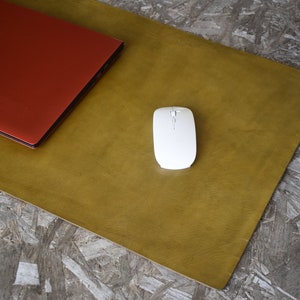 May include: A mustard yellow leather desk mat with a closed red laptop and a white wireless mouse on top.