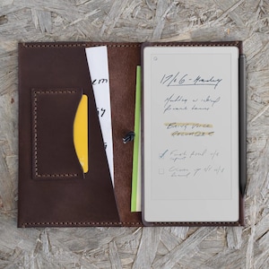 May include: A brown leather folio with a digital notepad and stylus. The notepad displays handwritten notes, including the date, "17/6 - Monday", and a to-do list. A yellow card and other papers are visible in the folio.