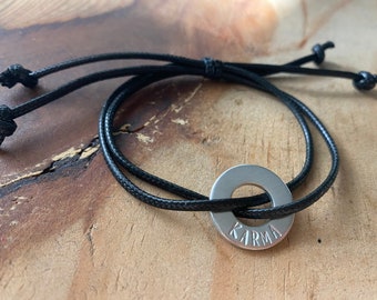 May include: A black cord bracelet with a silver metal charm that says "KARMA" on it.