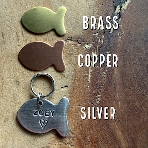 May include: Three fish-shaped metal tags in brass, copper, and silver. The silver tag has the name "ZOEY" engraved on it with a heart.