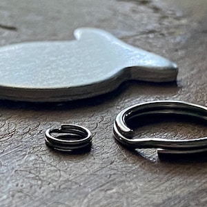 May include: Two silver key rings, one larger than the other, on a wooden surface. A white ceramic fish-shaped object is also on the surface.