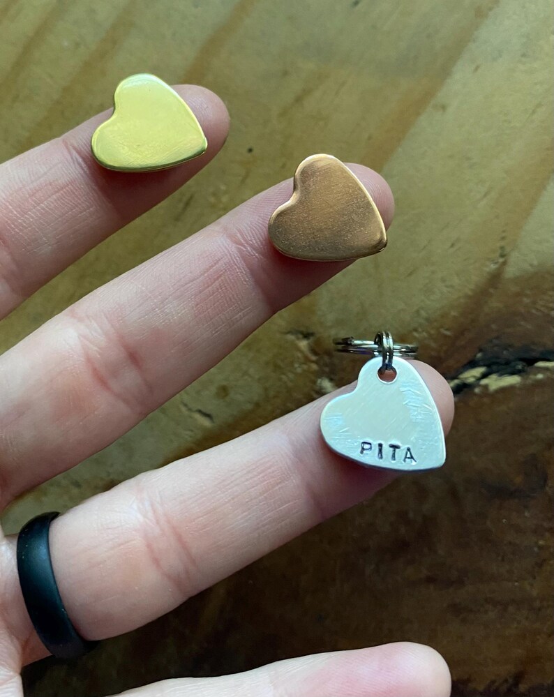 Pu&ograve; includere: Tre etichette di metallo a forma di cuore. Due sono lisce, una dorata e una in rame. La terza etichetta &egrave; in argento e ha il nome "PITA" inciso su di essa.