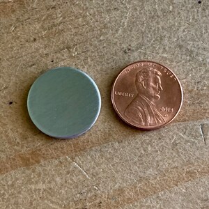 以下が含まれることがあります： 「In God We Trust」と「2014」の刻印がされた銅製のアメリカ1セント硬貨の隣に、銀色の金属製の円盤がある。