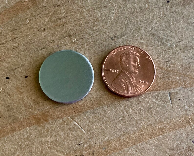 以下が含まれることがあります： 「In God We Trust」と「2014」の刻印がされた銅製のアメリカ1セント硬貨の隣に、銀色の金属製の円盤がある。