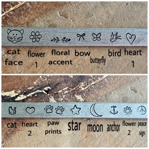 May include: A close-up of two rows of metal charms with various designs, including a cat face, flower, bow, butterfly, bird, heart, paw prints, star, moon, anchor, and peace sign. The charms are labeled with their names and quantities.