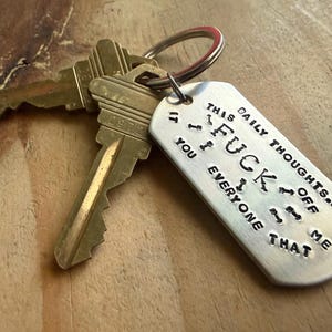 May include: A set of keys with a silver tag. The tag has the phrase "THIS DAILY THOUGHTS OFF ME YOU EVERYONE THAT" stamped on it. The keys are brass-colored and attached to a silver key ring.