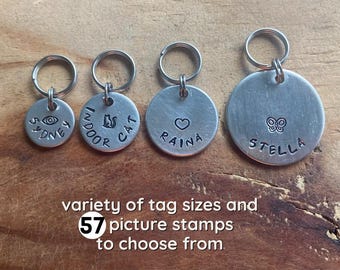 May include: Four silver keychains with different designs and names. The keychains have a variety of sizes and shapes. The keychains have the names Sydney, Indoor Cat, Raina, and Stella. The text "variety of tag sizes and 57 picture stamps to choose from." is below the keychains.