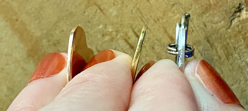Pu&ograve; includere: Due ciondoli a forma di cuore in metallo, uno dorato e uno argentato, sono tenuti tra due dita. Il ciondolo dorato &egrave; leggermente pi&ugrave; grande del ciondolo argentato.