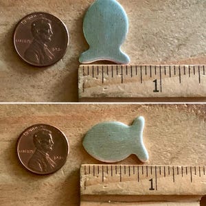 May include: Two light blue ceramic fish shapes, each about 1 inch long, are placed next to a ruler. The ruler is marked with inches.