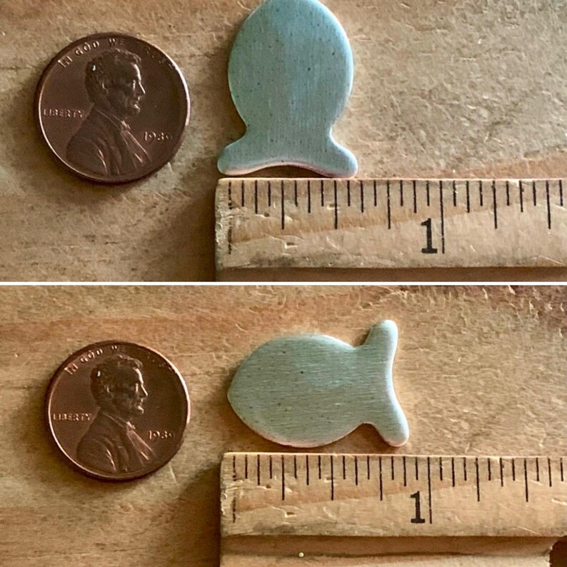 May include: Two light blue ceramic fish shapes, each about 1 inch long, are placed next to a ruler. The ruler is marked with inches.
