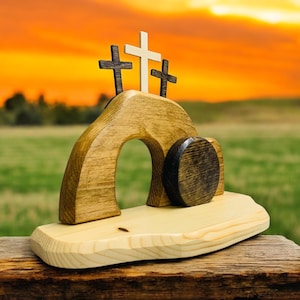 May include: Wooden Easter tomb with a rolling stone and three crosses. The tomb is painted brown and the crosses are painted black and white.