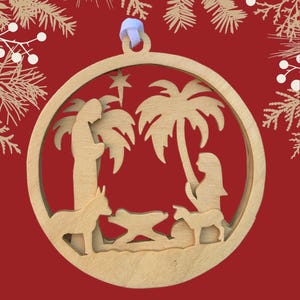 May include: A wooden Christmas ornament depicting the nativity scene with a star, palm trees, and figures of Mary, Joseph, and the baby Jesus in a manger. The ornament is circular and has a white ribbon for hanging.
