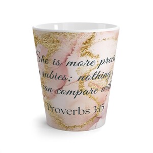 May include: A white ceramic mug with a pink and gold marble design. The mug features the text "She is more precious than rubies; nothing can compare with her." and "Proverbs 3:15".