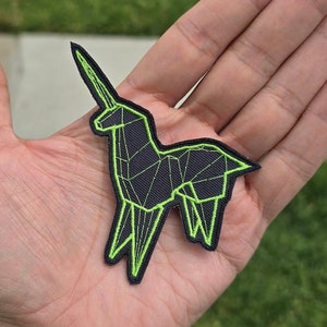 Könnte beinhalten: Ein gestickter Aufnäher in Schwarz und Grün, der ein Einhorn mit geometrischem Design zeigt.