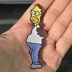 May include: Yellow embroidered patch of a cartoon character with a yellow head, white shirt, blue jeans, and black shoes.