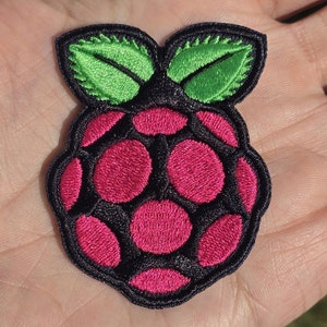 Könnte beinhalten: Ein gestickter Patch in Pink und Schwarz, der wie eine Himbeere mit grünen Blättern geformt ist. Der Patch ist ein beliebtes Symbol für den Raspberry Pi-Computer.
