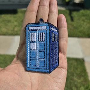 Könnte beinhalten: Ein blauer und weißer gestickter Aufnäher einer Polizeikabine, ein bekanntes Motiv aus der britischen Science-Fiction-Fernsehserie Doctor Who.