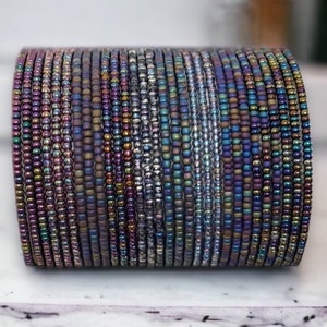 May include: A stack of iridescent beaded bracelets in shades of purple, blue, and silver. The bracelets are made of small, round beads that are strung together to create a continuous loop.