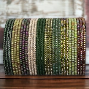 May include: A stack of green, brown, and cream colored beaded bracelets. The bracelets are made of small, round beads and are arranged in a vertical stack.