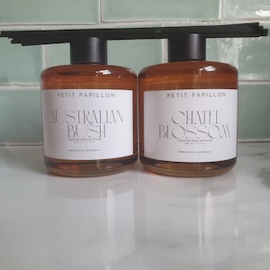 May include: Two glass reed diffusers with black caps and reeds. The labels read "PETIT PAPILLON AUSTRALIAN BUSH" and "CHATEL BLOSSOM". Each diffuser contains 100 ml / 3.4 fl oz of scented oil. The text "NEWCASTLE, AUSTRALIA" is also visible.