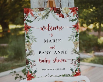 May include: A wooden easel displays a baby shower welcome sign. The sign features the words "welcome to MARIE and BABY ANNE baby shower" in red script, surrounded by a floral border with red poinsettias and greenery. The date "DECEMBER 21ST, 2023" is at the bottom.