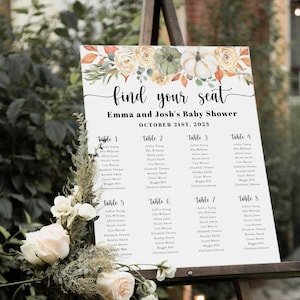 Puede incluir: Un letrero blanco sobre un caballete con el texto "find your seat" y "Emma and Josh's Baby Shower October 21st, 2023". El letrero tiene ilustraciones florales y de calabazas y enumera las asignaciones de mesa.