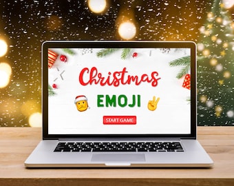 May include: A laptop computer with a white screen displaying a Christmas Emoji game. The screen has a red and white Christmas theme with a green tree and a red gift box. The text on the screen reads "Christmas Emoji" and "Start Game". The laptop is on a wooden table with a blurry background of a Christmas tree and lights.