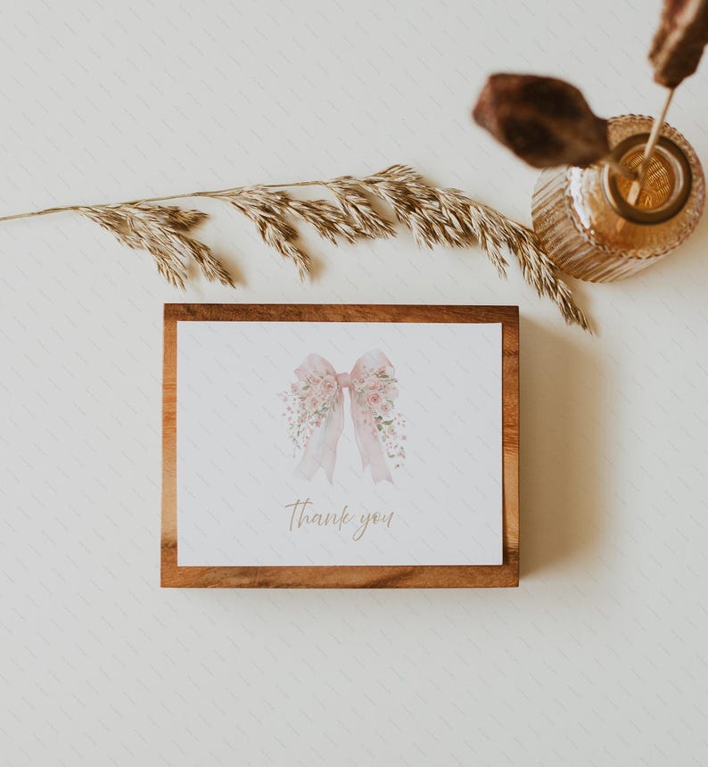 Pode incluir: Cart&atilde;o retangular emoldurado em madeira, com um desenho de la&ccedil;o em aquarela com detalhes florais. O la&ccedil;o &eacute; rosa claro com fitas e pequenas flores. As palavras "Thank you" s&atilde;o escritas em uma caligrafia elegante.