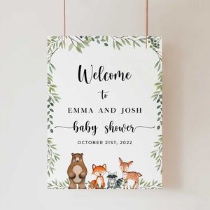 May include: Welcome to Emma and Josh's baby shower sign with a leafy green border and woodland animal illustrations. The sign says "Welcome to Emma and Josh baby shower October 21st, 2022".