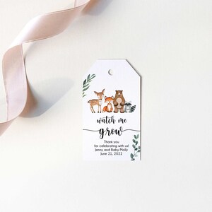 May include: A white tag with a green leafy border and a watercolor illustration of a deer, fox, bear, and raccoon. The text "watch me grow" is written in black cursive font. The text "Thank you for celebrating with us! Jenny and Baby Molly June 21, 2022" is written in black font.