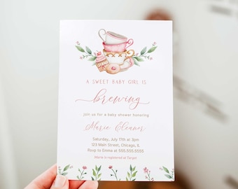 Puede incluir: Una invitación a un baby shower con un diseño de acuarela. La invitación presenta tazas apiladas, una magdalena y una rosquilla. El texto dice "A Sweet Baby Girl Is Brewing" y los detalles del evento. La invitación es sostenida por una mano.