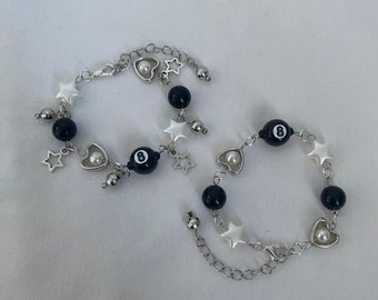 May include: Two silver chain bracelets with black and white charms. The charms include stars, hearts, and 8-ball designs.