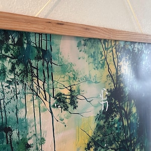 Puede incluir: Una impresi&oacute;n enmarcada de una pintura de acuarela que representa una escena de bosque con tonos verdes y amarillos. La pintura presenta un solo personaje blanco en la esquina inferior derecha.