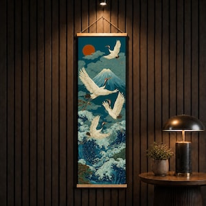 Könnte beinhalten: Ein vertikaler Wandbehang mit einer detaillierten Illustration von vier weißen Kranichen, die über aufgewühlten blauen Meereswellen fliegen. Im Hintergrund erhebt sich ein schneebedeckter Berggipfel unter einer dunkelorangen Sonne und stilisierten Wolken.