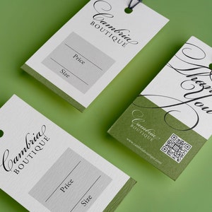 May include: Two white gift tags with black text. The top tag says "Cambria Boutique" and "Thank You" in cursive. The bottom tag says "Cambria Boutique" and has a blank space for "Price" and "Size".