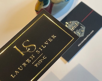 May include: A black business card with gold foil lettering. The text reads "LS Lauren Silver FNT-C".