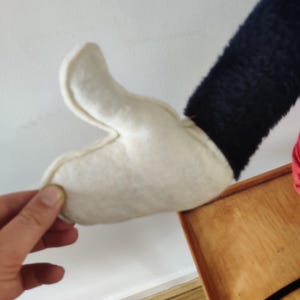 K&ouml;nnte beinhalten: Ein wei&szlig;er Filzhandschuh mit einem schwarzen &Auml;rmel, m&ouml;glicherweise Teil eines Kost&uuml;ms oder eines Pl&uuml;schtiers. Der Handschuh wird von einer Hand gehalten, die die Details der N&auml;hte und des Materials zeigt.