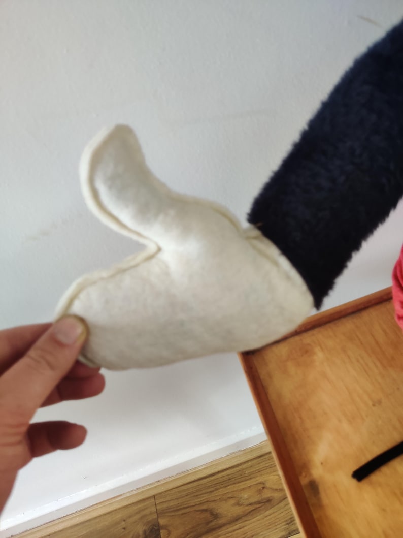 K&ouml;nnte beinhalten: Ein wei&szlig;er Filzhandschuh mit einem schwarzen &Auml;rmel, m&ouml;glicherweise Teil eines Kost&uuml;ms oder eines Pl&uuml;schtiers. Der Handschuh wird von einer Hand gehalten, die die Details der N&auml;hte und des Materials zeigt.