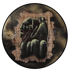 May include: A round decorative plate featuring an Egyptian pharaoh profile and bird design in shades of black, brown, and gold. The artwork is set against a textured, light brown background, framed by a black border.