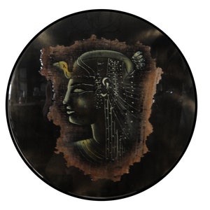 May include: Round decorative piece featuring an Egyptian pharaoh profile. The artwork is set against a dark background, framed by a black border. The pharaoh's profile is detailed with gold and green accents, set on a textured, aged paper.