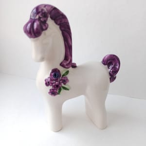 May include: White ceramic horse figurine with purple mane and tail, decorated with purple flowers.