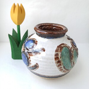 Könnte beinhalten: Eine kleine weiße Keramikvase mit braunem Rand und einem dekorativen Design aus blauen, grünen und braunen Wirbeln.