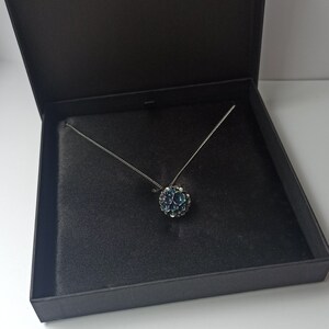 Pode incluir: Um colar de corrente de prata com um pingente de pedra preciosa azul em uma caixa forrada de veludo preto.