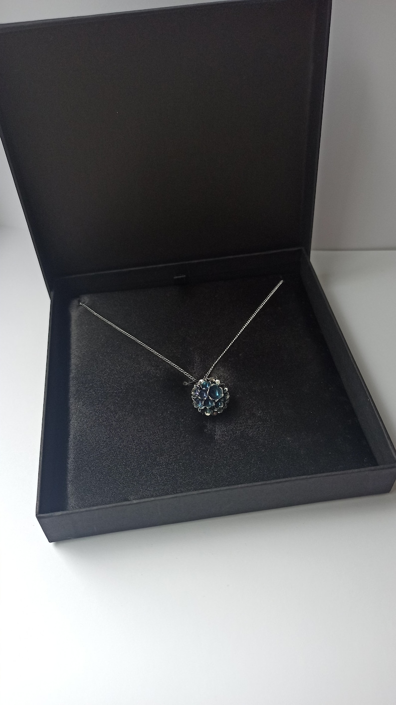 Pode incluir: Um colar de corrente de prata com um pingente de pedra preciosa azul em uma caixa forrada de veludo preto.